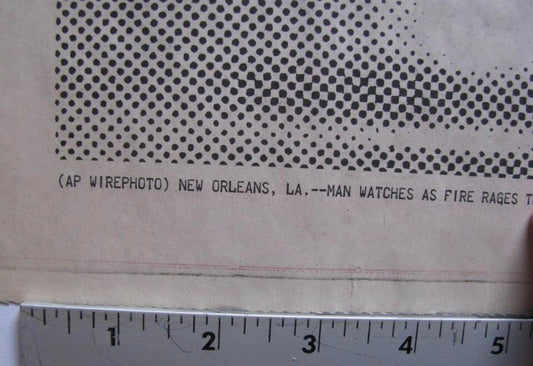 A close-up of a vintage printed paper item showing a halftone dot pattern and a partial news caption, with a metal ruler along the bottom edge for scale.