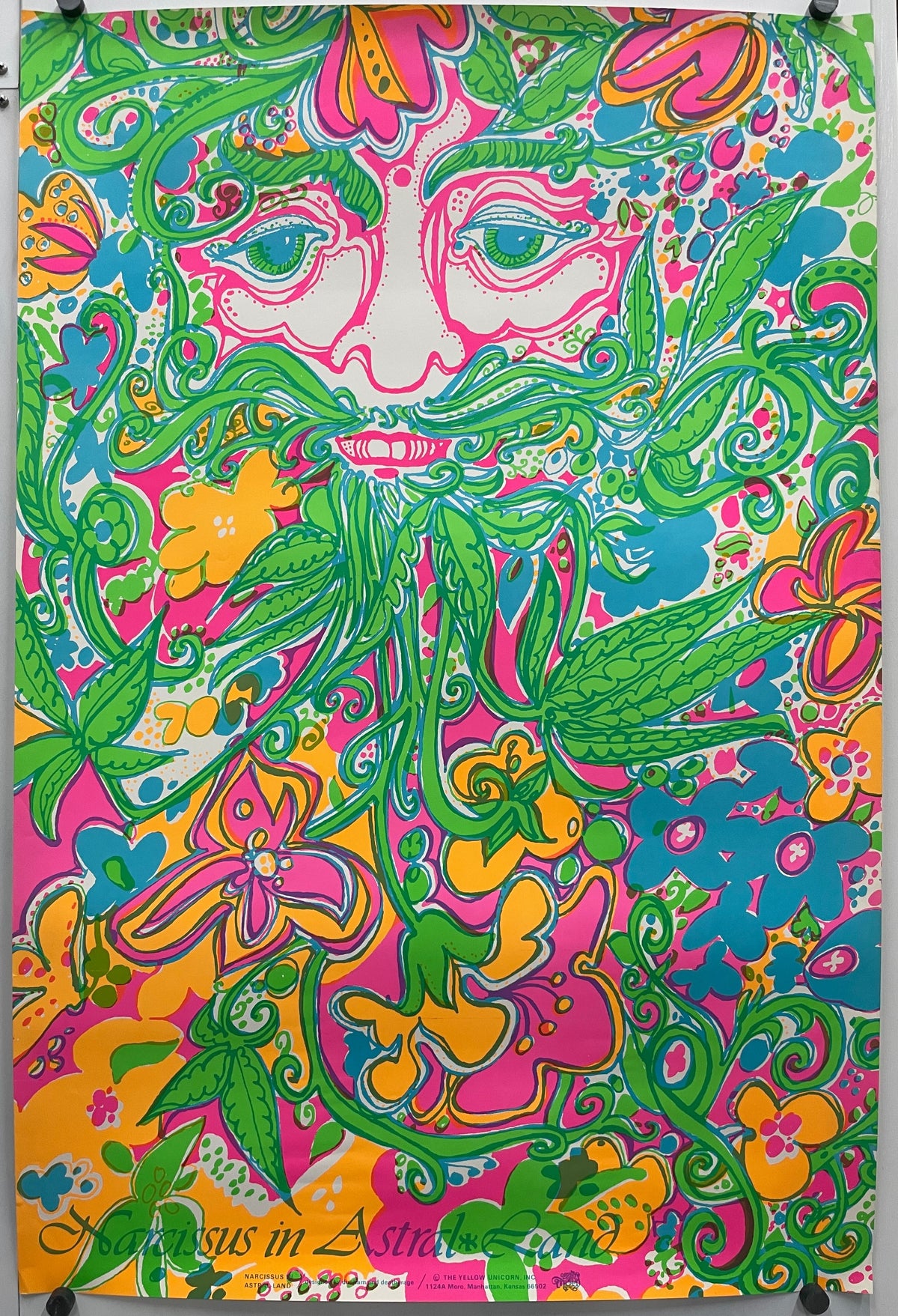 A rectangular panel featuring a vibrant, psychedelic floral and paisley pattern in pink, green, yellow, and blue, displayed flat with binder clips at the corners for a 1960s Narcissus in Astral Land.