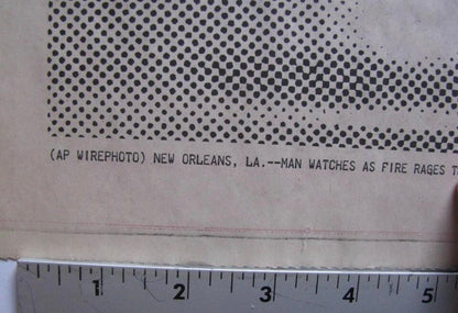A close-up of a vintage printed paper item showing a halftone dot pattern and a partial news caption, with a metal ruler along the bottom edge for scale.