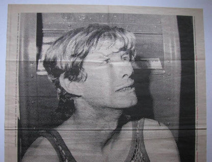 A black and white halftone portrait print of a survivor looking upward, shown against a light beige background with visible fold lines.