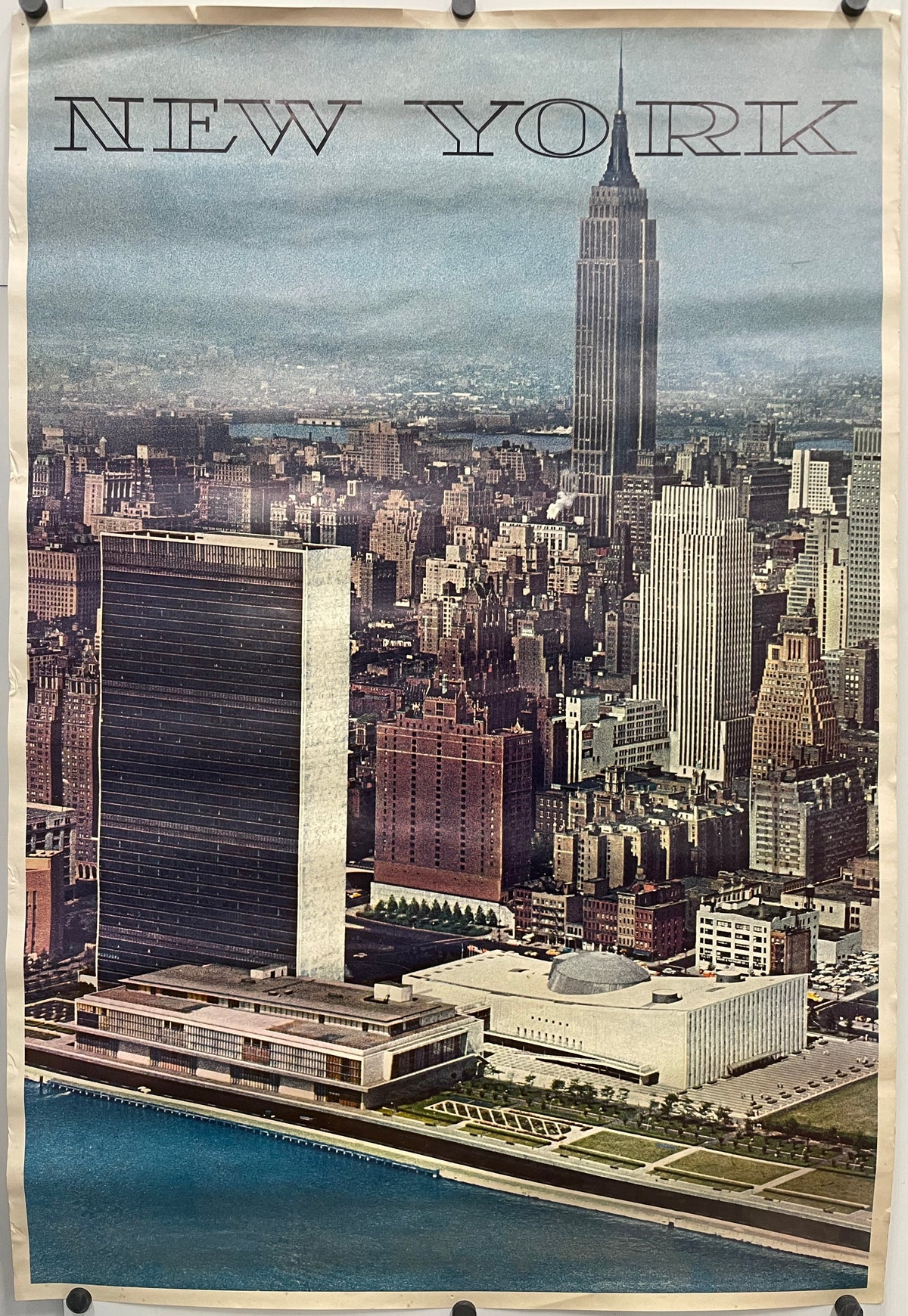 AERIAL VIEW MIDTOWN MANHATTAN SKYLINE FROM EAST RIVER LOOKING WEST UNITED NATIONS AND EMPIRE STATE BUILDINGS. New York text is printed at the top of the image of the city against a gradient blue background.