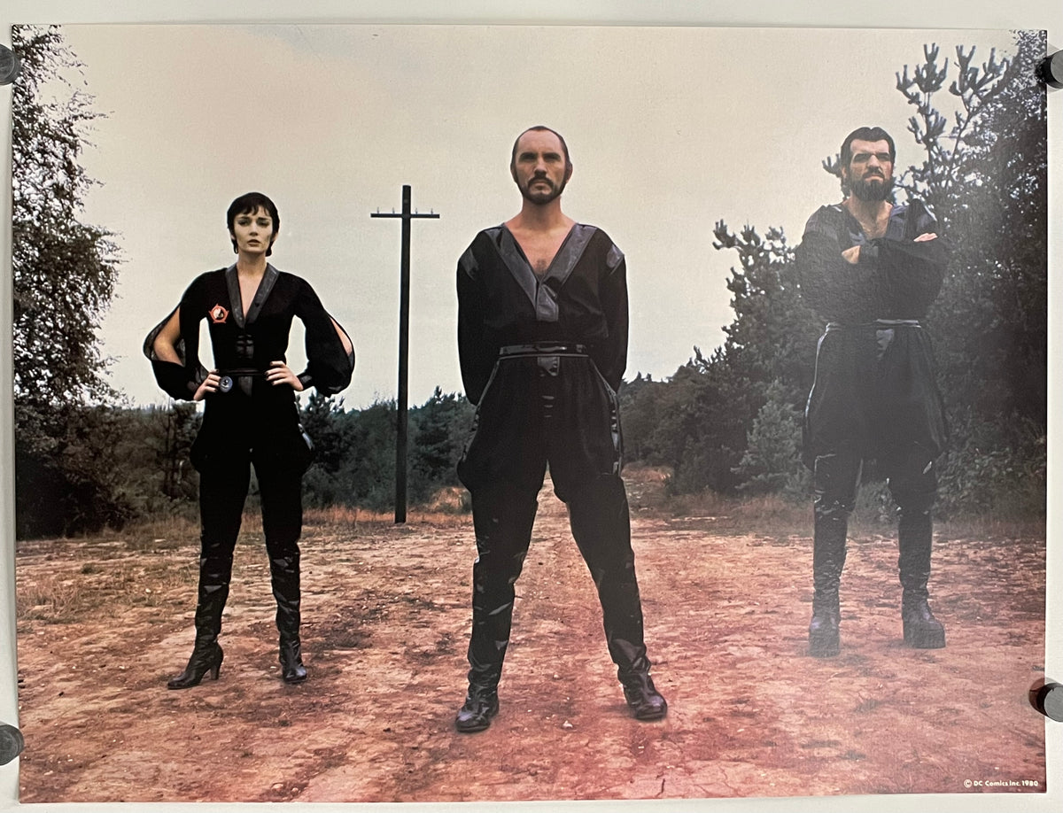 Three people in dark clothing standing in a forest with a cross in the background