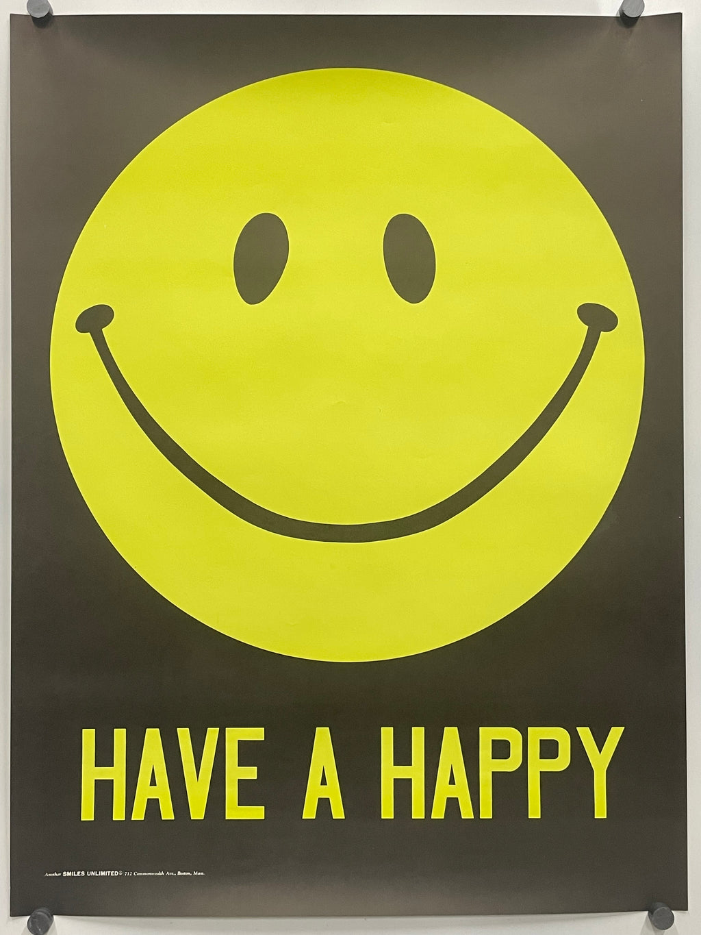 A black poster featuring a large yellow smiley face and the words 'HAVE A HAPPY' in yellow, hung with visible wall anchors.