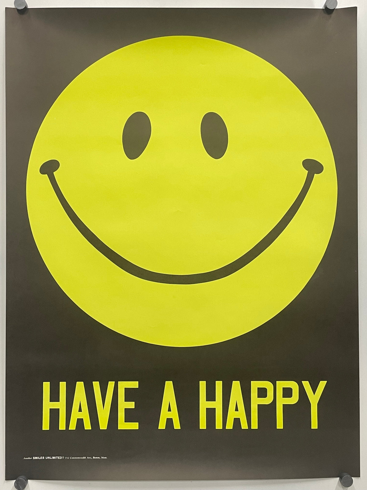 A black poster featuring a large yellow smiley face and the words 'HAVE A HAPPY' in yellow, hung with visible wall anchors.