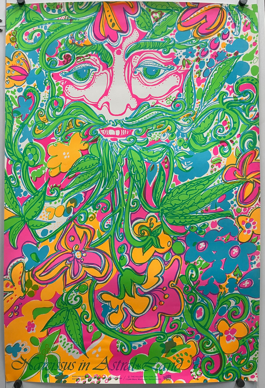 A rectangular panel featuring a vibrant, psychedelic floral and paisley pattern in pink, green, yellow, and blue, displayed flat with binder clips at the corners for a 1960s Narcissus in Astral Land.