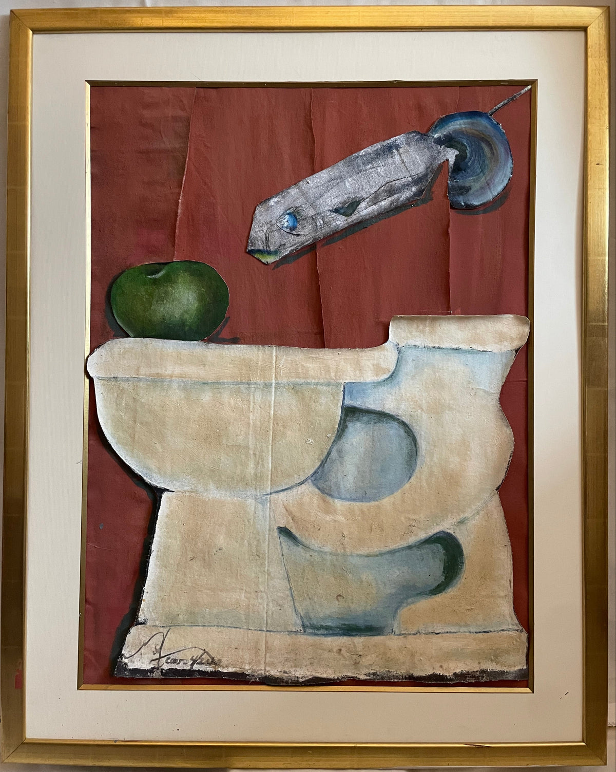 A framed abstract still life collage  featuring a red-brown background with a gray fish, a green apple, and cream-colored toilet, enclosed in a gold frame with an off-white mat.