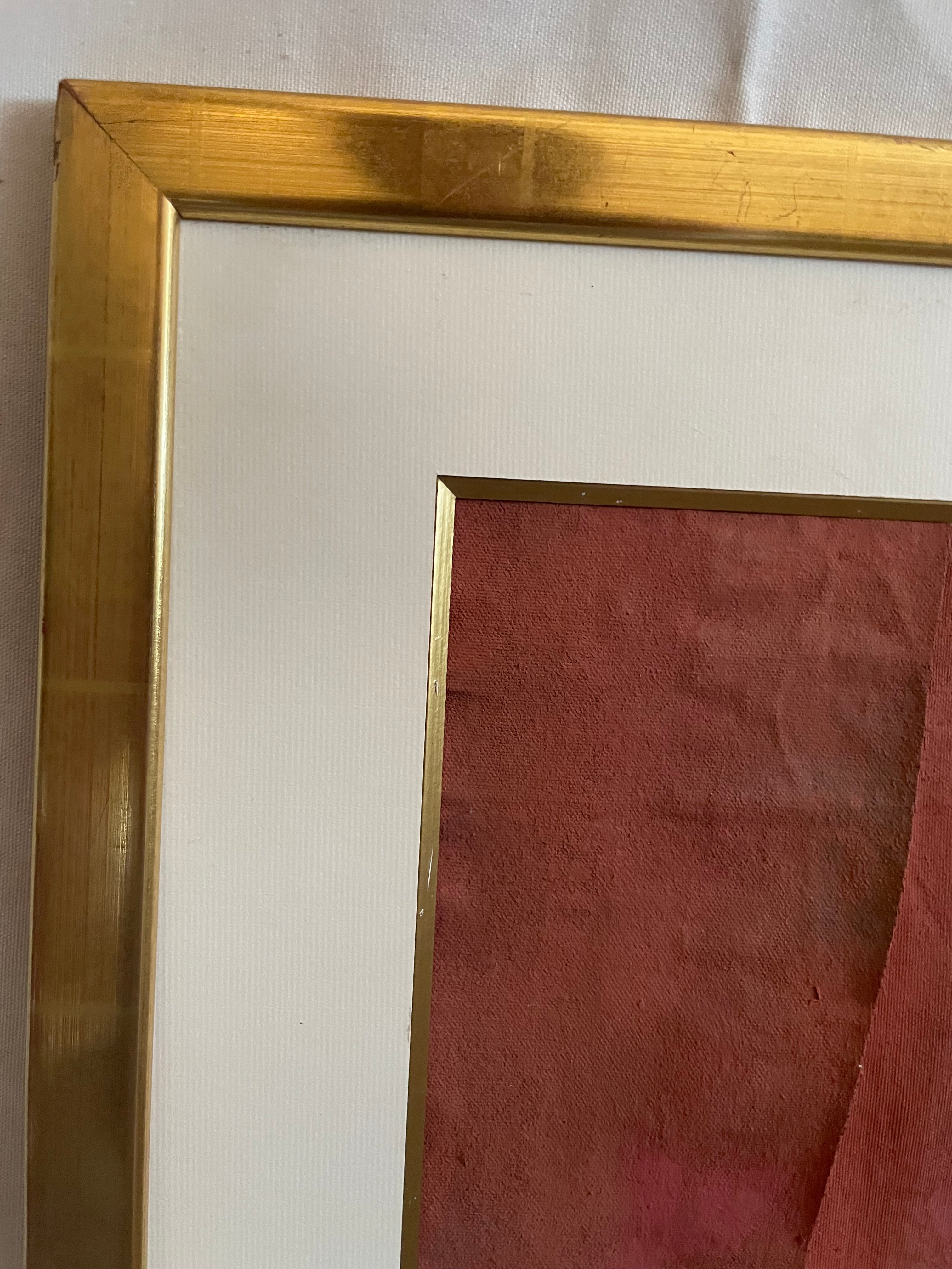 Close-up of a framed art print showing a gold metal frame, white mat board, and a reddish-brown textured paper background.