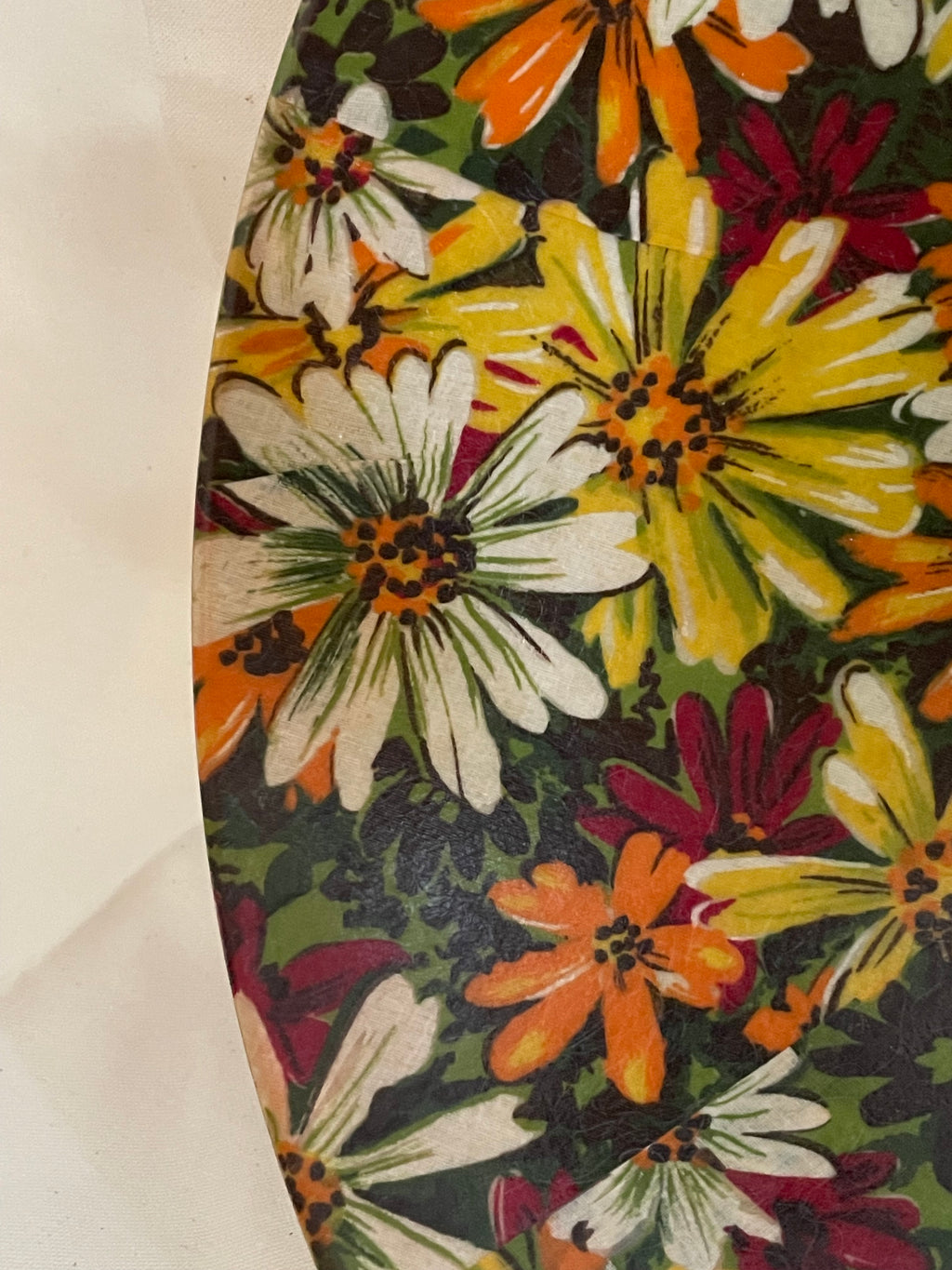A close-up of a vintage floral pattern, featuring large daisy-like flowers in yellow, orange, white, and burgundy on a dark green background.