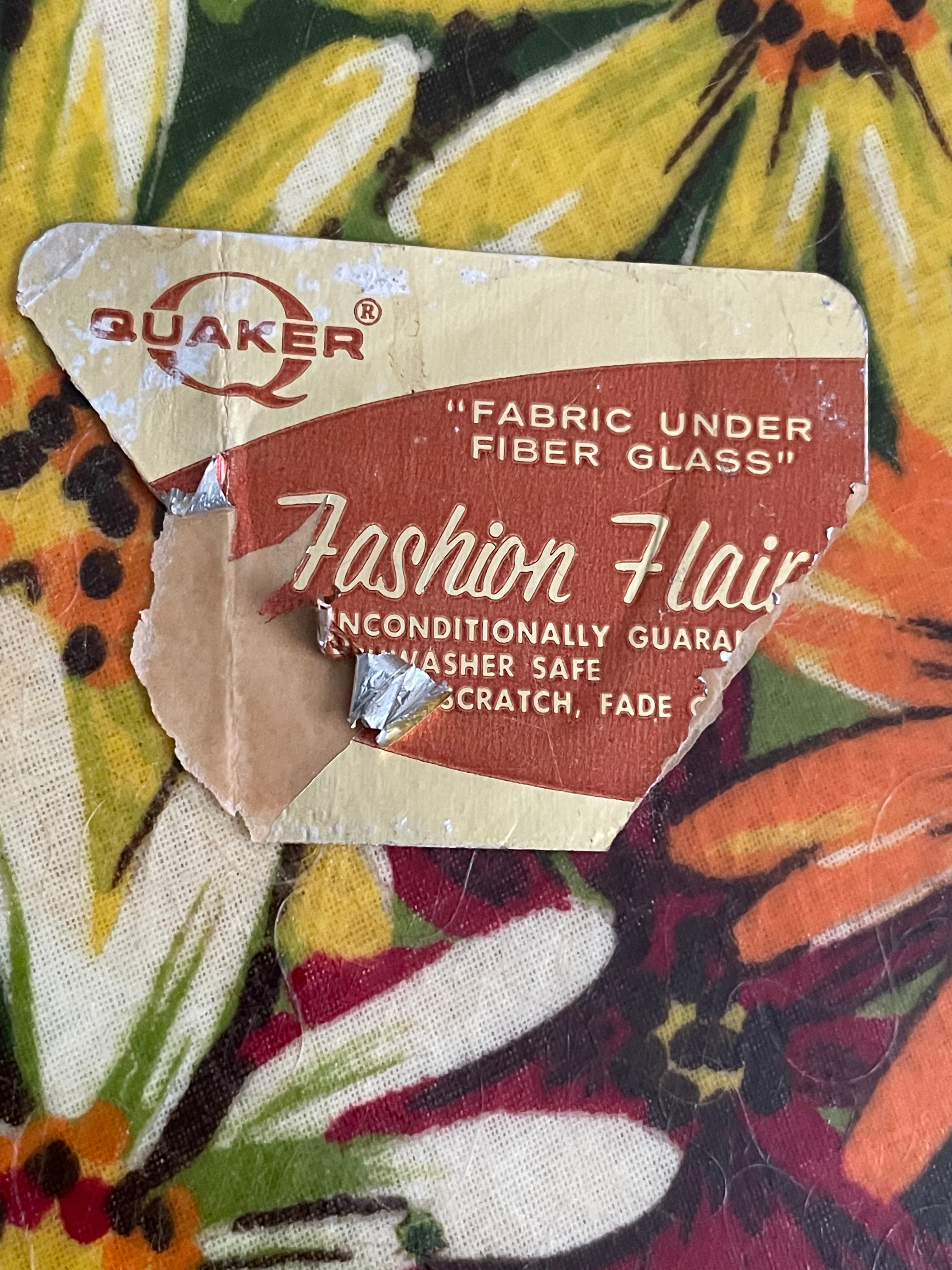 A torn vintage Quaker Fashion Flair fabric under fiber glass label placed on a colorful floral patterned textile background.