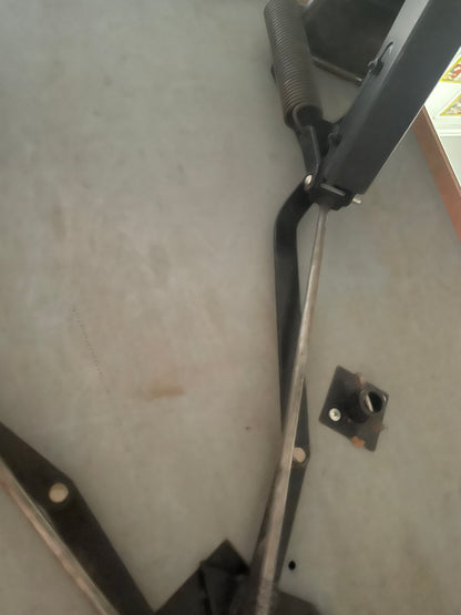A close-up view of a black metal mechanical component with a spring and long rod on a gray concrete floor.