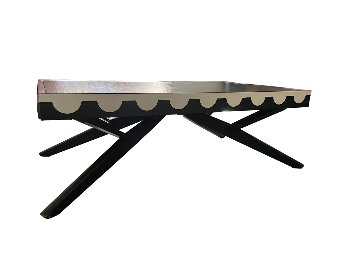 A mid-century modern coffee table with a black X-frame base and a scalloped cream top, shown in a living room setting.